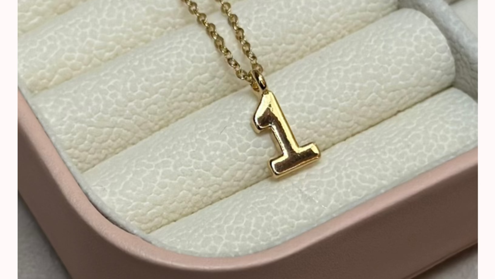 Gold necklace with a '1' pendant on a textured surface, branded 'CYPHER'.