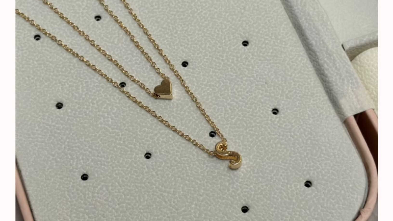 Gold necklaces with heart and 'S' charm on a display stand with 'Emblem Necklace' text.